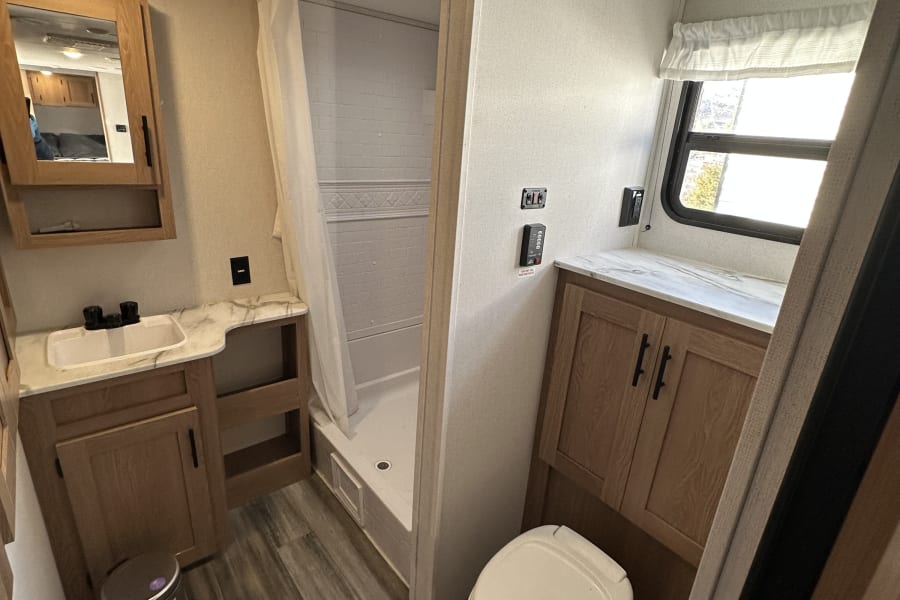 This RV rental features a modern and functional bathroom with a shower, toilet, sink, mirror, and cabinet storage.