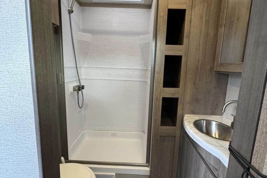 RV rental bathroom featuring a compact stand-up shower, toilet, and vanity with a sink. Practical interior for travel.