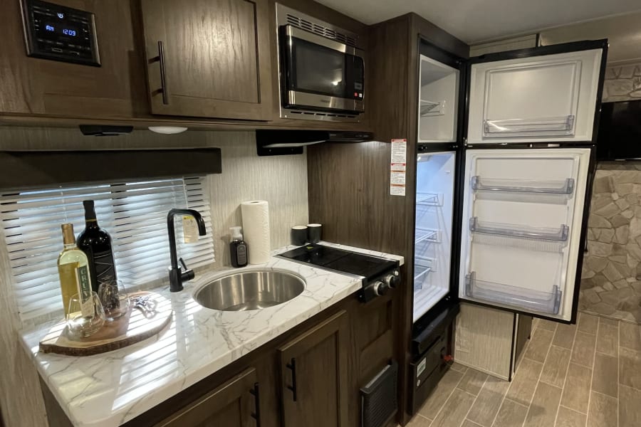 Explore this inviting rv rental kitchen, boasting a sink, stovetop, microwave, open refrigerator, and stylish wood finishes.