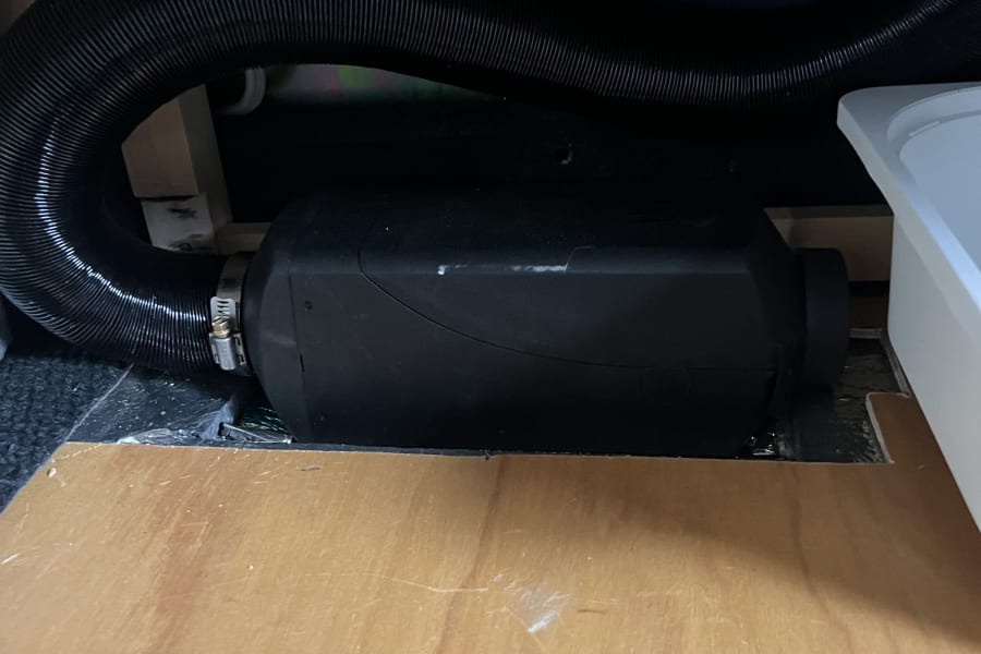 Compact black diesel heater and its air duct, installed in an RV rental for effective heating.