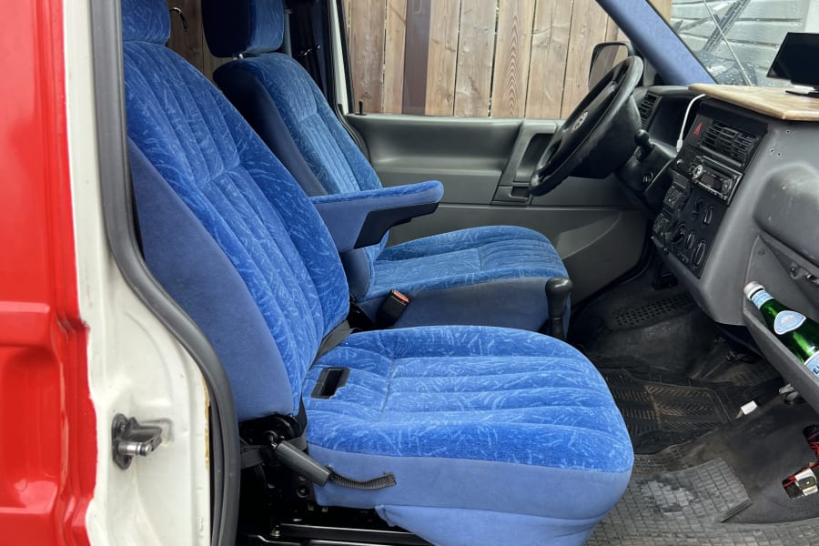 Inside this RV rental: blue upholstered front seats, dashboard, and overhead storage visible from the open passenger door.