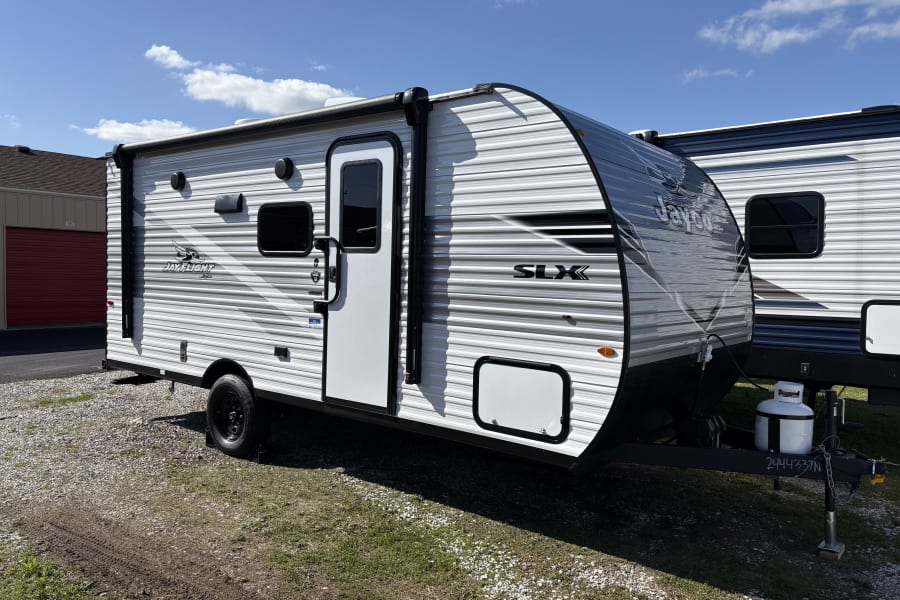New white Jayco Jay Flight SLX travel trailer, a perfect RV rental option, awaits adventure under a sunny sky.