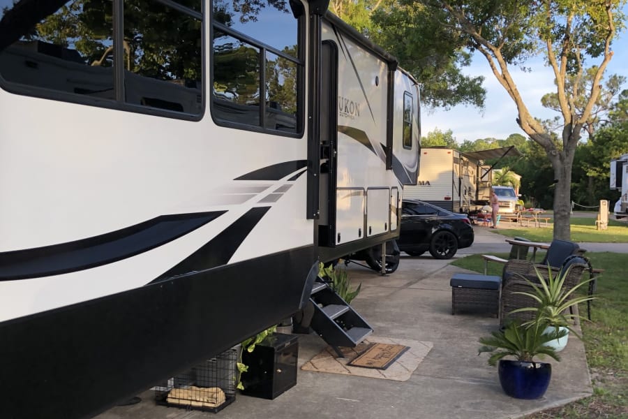 Spacious RV rental parked at a serene campground, featuring outdoor living space with furniture and greenery.