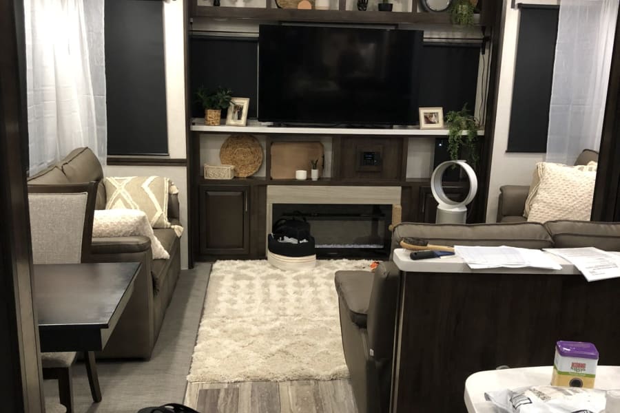 RV rental interior: A modern living space with comfy sofas, TV, fireplace, and light wood flooring, creating a cozy atmosphere.