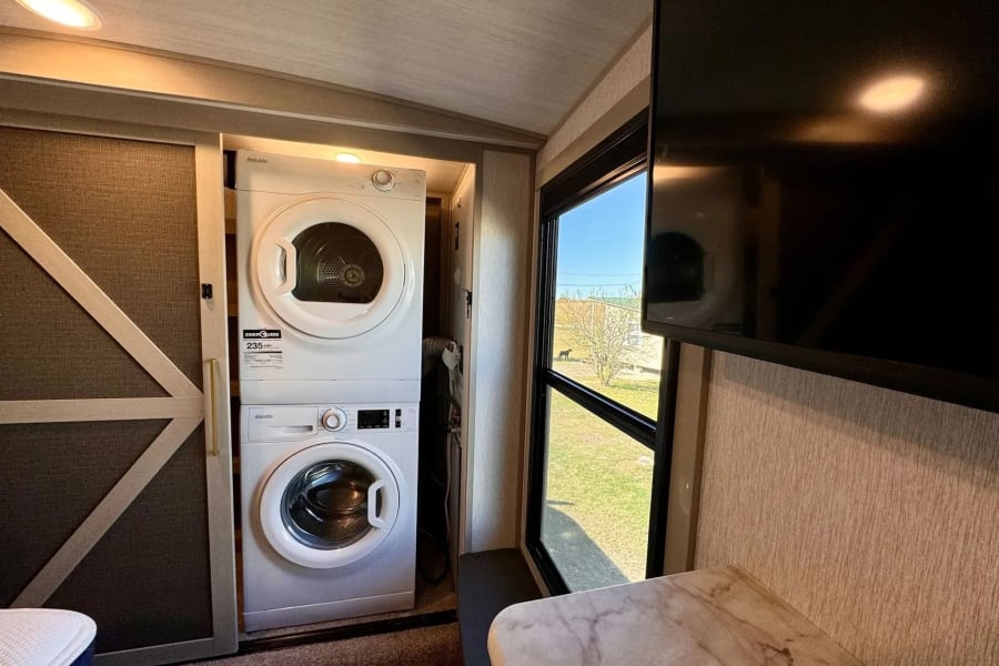 Inside this RV rental: a compact stacked washer/dryer, TV, and window view, offering home comforts for travel.