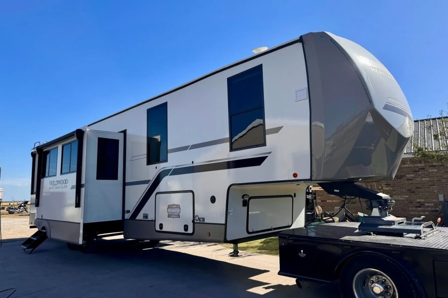 Large, white and gray Wildwood Heritage Glen fifth-wheel RV for rv rental, hitched to a truck on a sunny day.