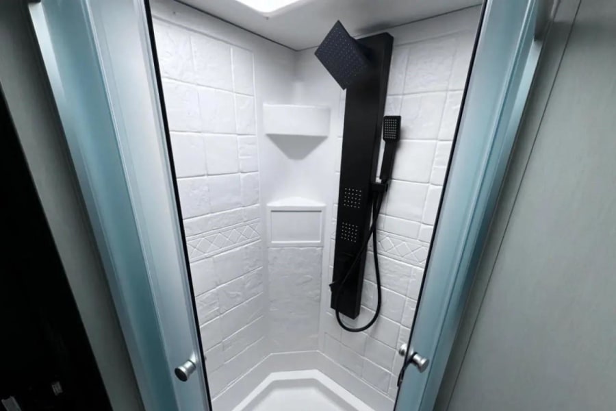 This modern RV rental features a clean, hexagonal shower with white textured walls and a sleek black shower panel.
