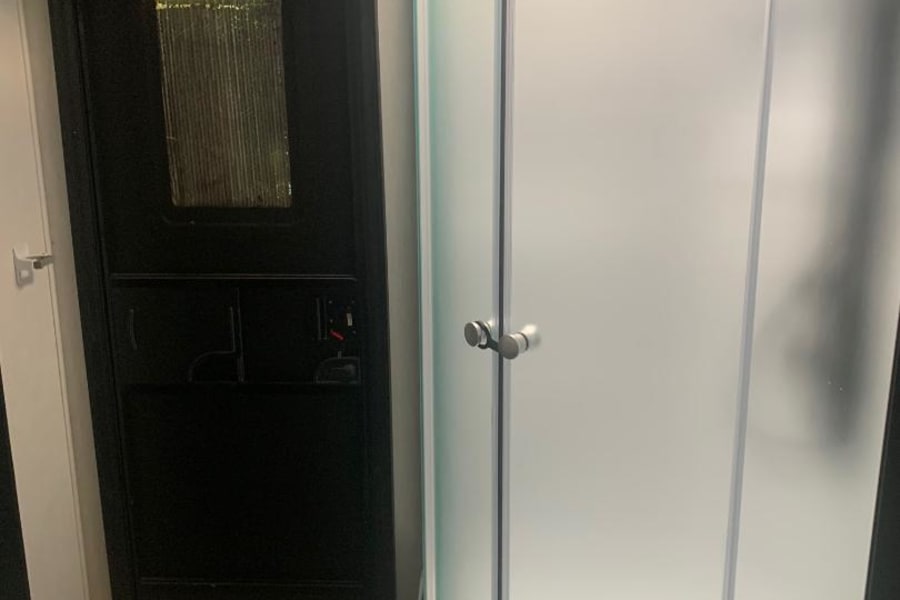 Inside this RV rental: a compact bathroom with a curved, frosted shower stall, toilet, and a dark door.