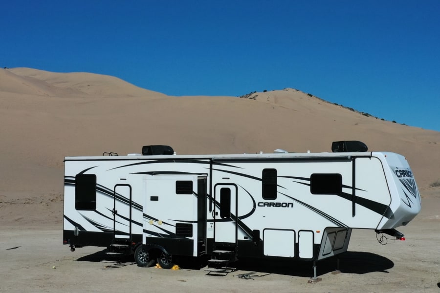 This Carbon fifth-wheel RV rental is perfectly set up for adventure among vast desert sand dunes under a clear sky.