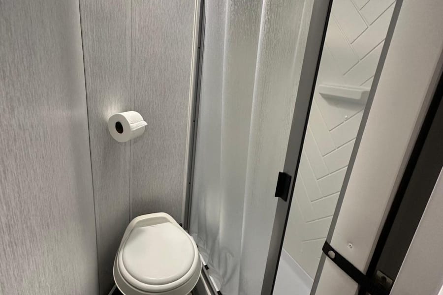 Inside an RV rental bathroom: a white toilet, toilet paper, and a curved, textured shower curtain defining the compact shower space.
