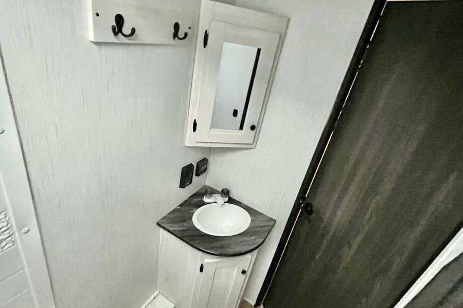 Compact RV rental bathroom features a corner sink vanity, mirrored cabinet, toilet, and shower area.
