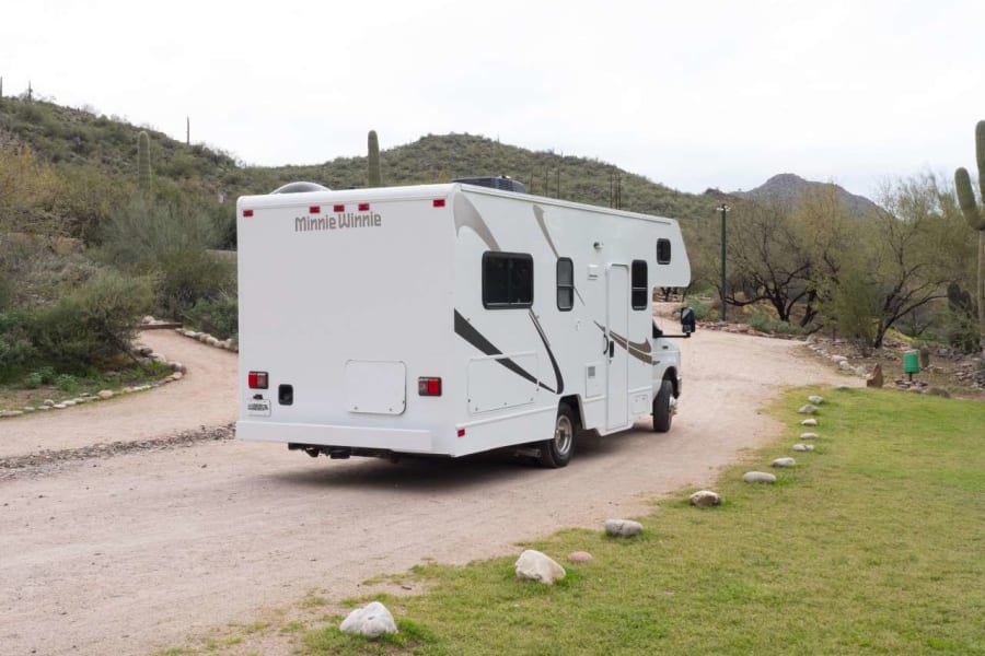 Minnie Winnie rv rental parked on a desert dirt road with saguaro cacti, perfect for adventure travel.