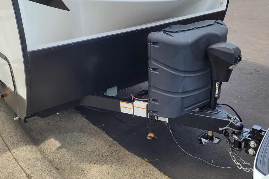 Close-up of a white travel trailer (RV rental) front, showing black propane tanks and hitch.