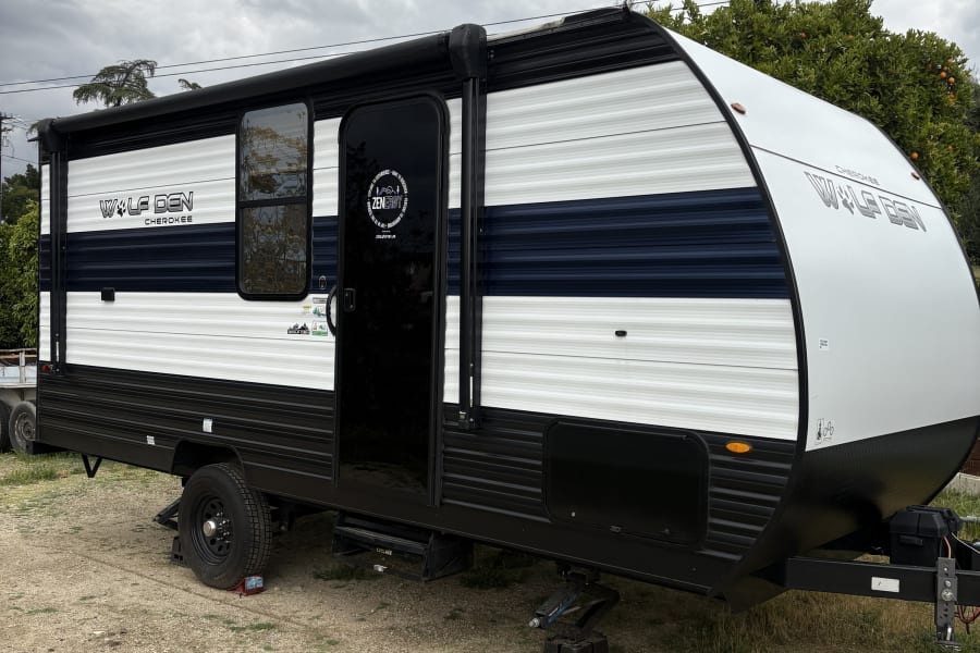 A black and white Wolf Den Cherokee travel trailer parked on a gravel lot under cloudy skies, perfect for an rv rental adventure.