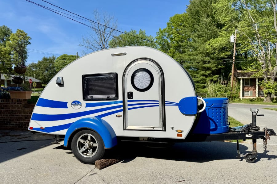 White & blue T@G teardrop camper, great for an rv rental. Parked outside on a sunny day, ready for adventure.