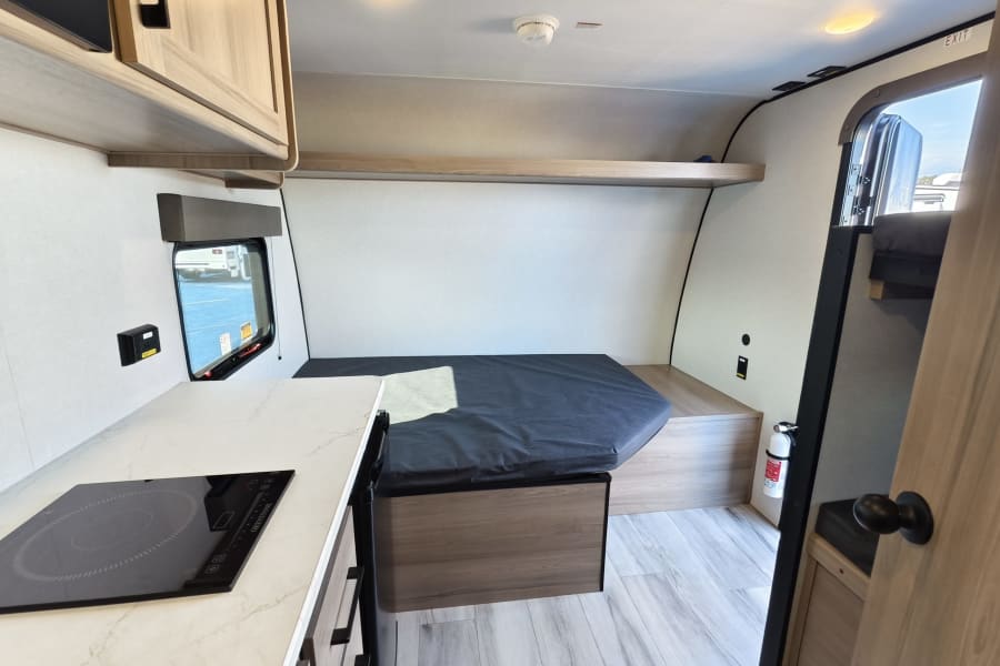 Compact RV rental interior featuring a kitchen with cooktop, sleeping area, and overhead storage, ideal for adventure.