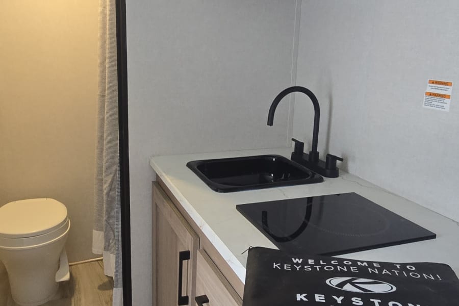 RV rental interior features a modern, compact kitchen with a sink, cooktop, microwave, fridge, and adjacent bathroom.
