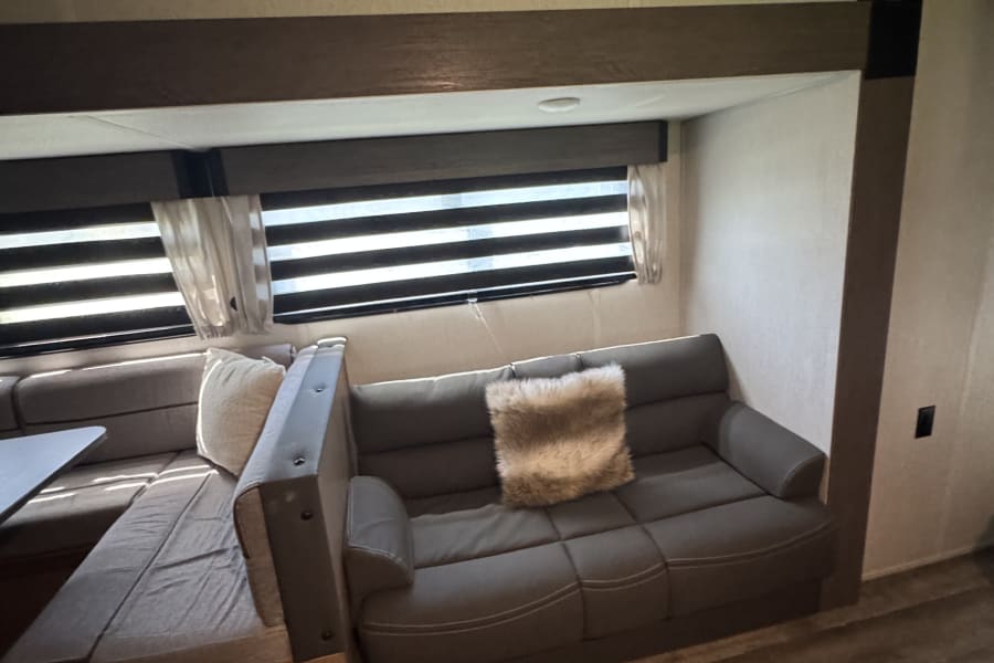 Cozy RV rental interior: comfortable sofa, dinette seating, wood floors, and windows with blinds.