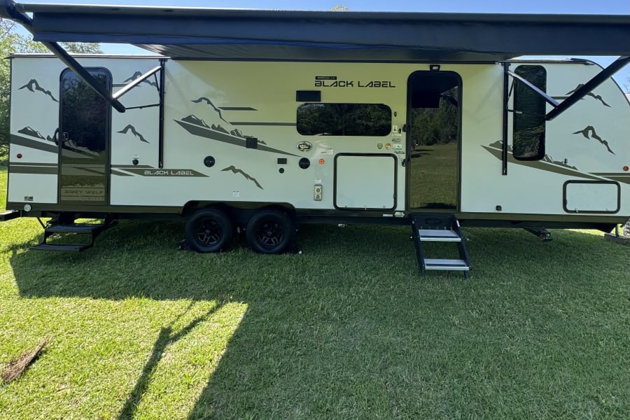 RV rental: This Grey Wolf Black Label travel trailer, with extended awnings and steps, is ready for outdoor adventures on green grass.