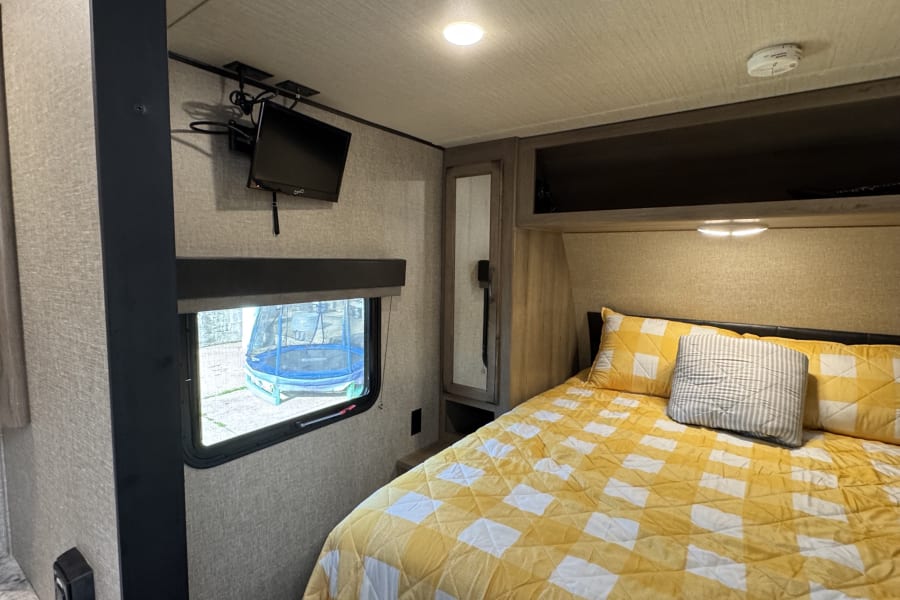 Cozy RV rental bedroom with checkered bed, window view of a trampoline, and wall-mounted TV.