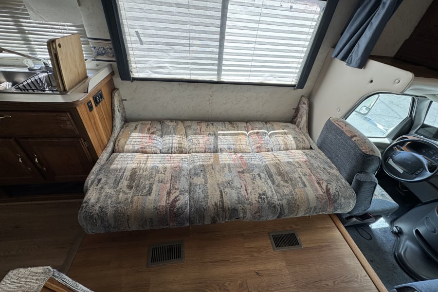 Cozy RV rental interior showcasing a patterned sofa, kitchen counter, and the driver's cab for travel comfort.