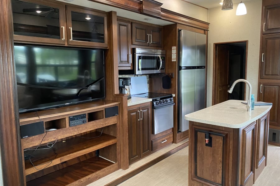 Spacious RV rental interior with a well-equipped kitchen island, entertainment center, and modern appliances.