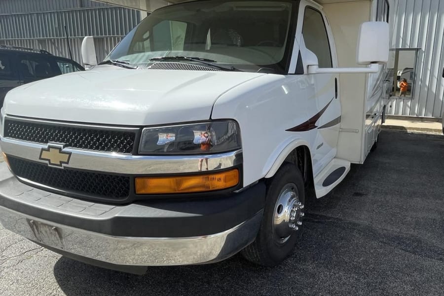 White Coachmen Freelander Class C RV rental, full front view. Parked on asphalt under clear sky.