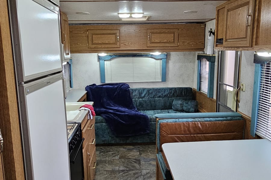 View of an RV rental interior, showing kitchen with fridge/stove, dinette, and living area with sofa and teal upholstery.