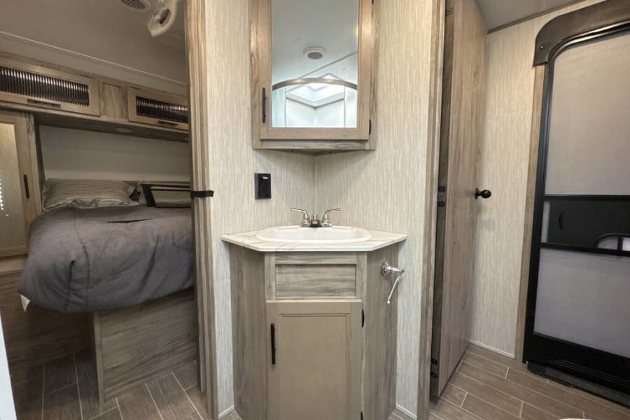 An RV rental interior with a cozy bedroom, corner sink vanity, and adjacent bathroom space.
