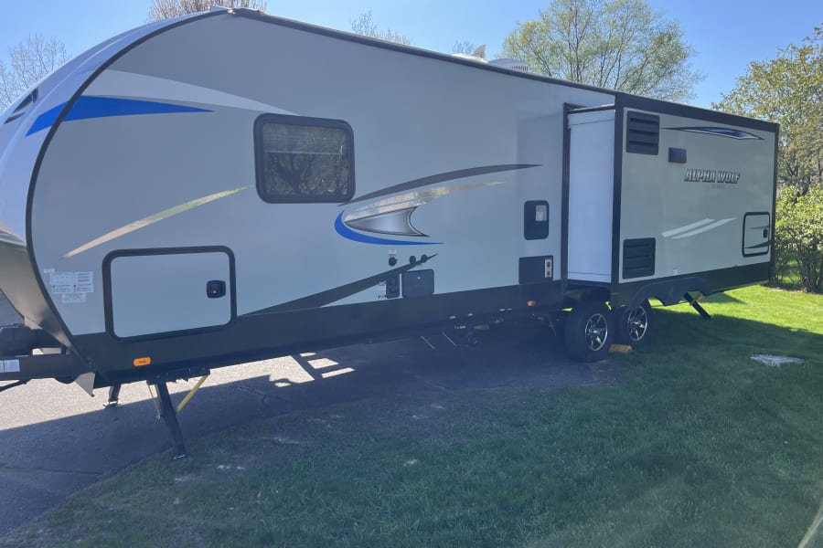 Spacious Alpha Wolf rv rental travel trailer with an extended slide-out at a sunny campsite.