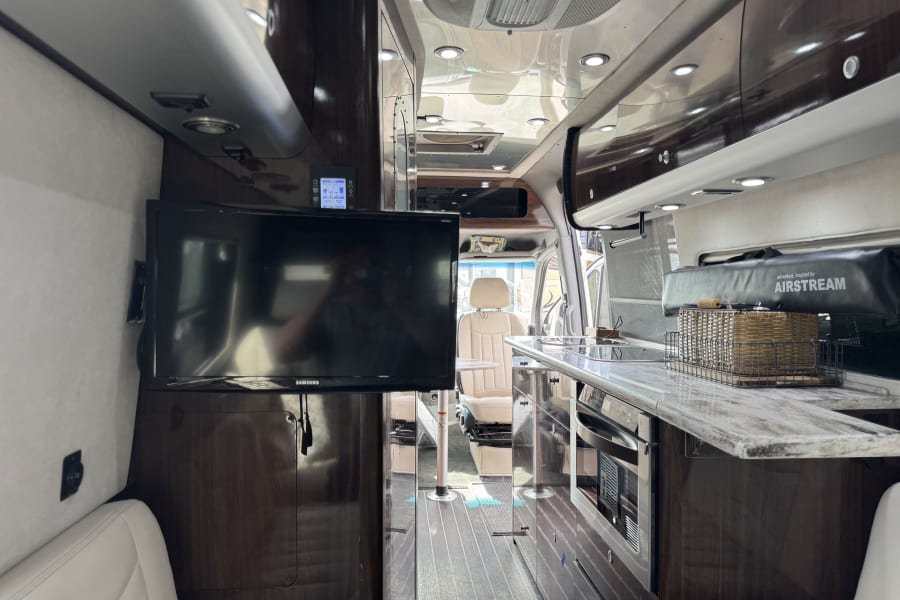Step inside this elegant Airstream RV rental, showcasing a TV, a well-equipped kitchen, and plush seating.