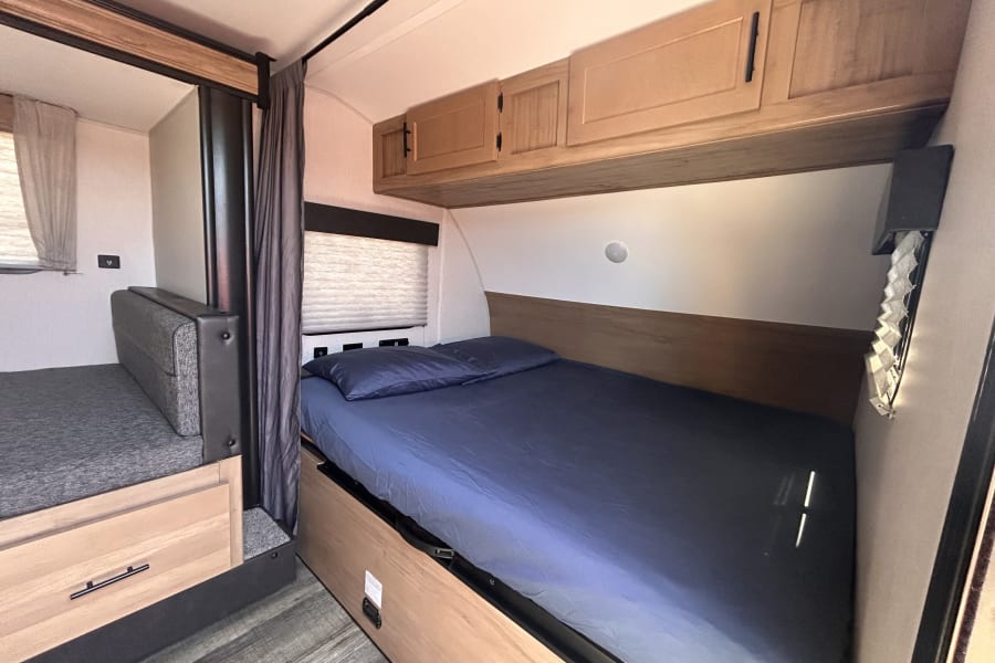 Cozy RV rental interior with a main bed, extra sleeping area and drawer, plus overhead cabinets for compact living.