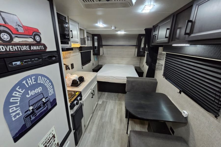 This RV rental's interior features a compact kitchen, dining area with table, and a comfortable bed for road trip adventures.