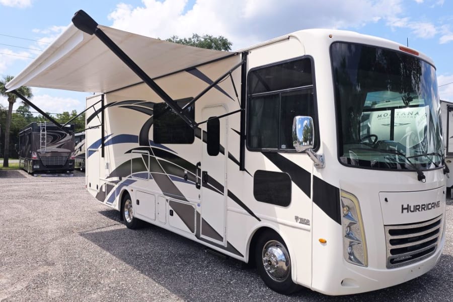 RV rental: White Hurricane motorhome with extended awning, on a gravel lot. Ideal for outdoor adventures.
