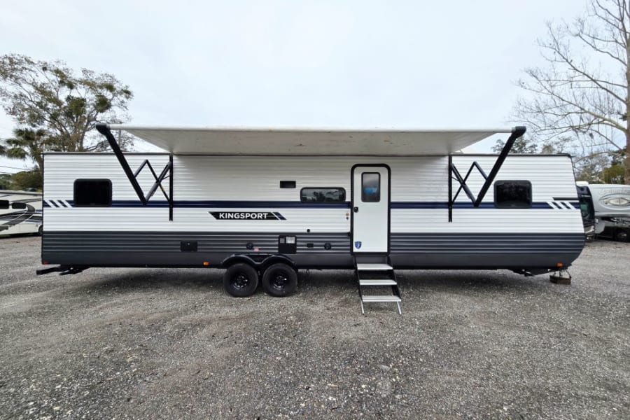 This white & gray Kingsport travel trailer, perfect for an RV rental, features an extended awning & entry steps.