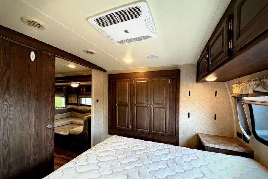 Explore this RV rental's functional interior: a cozy bedroom featuring a mattress, ample storage, and views into the connected living area.