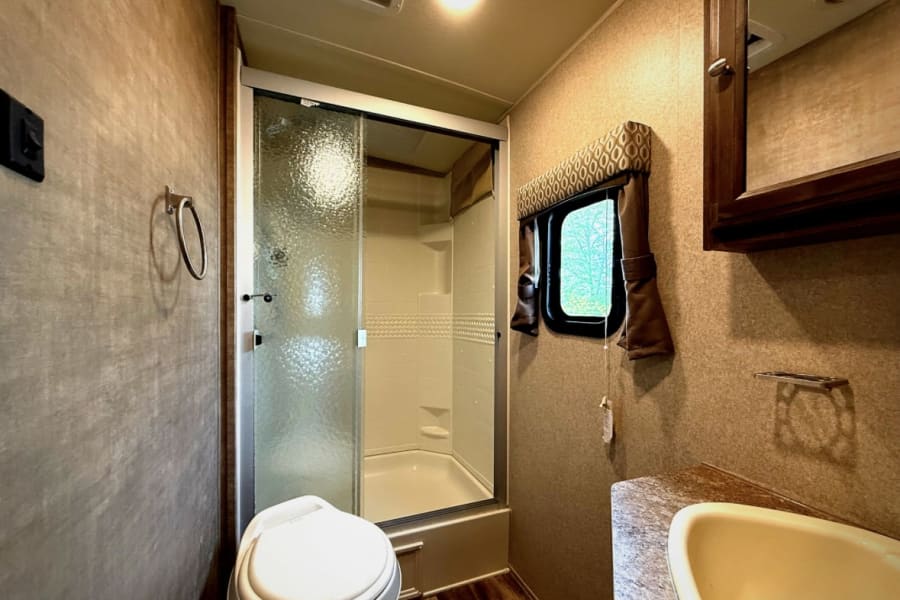 RV rental bathroom: Spacious with corner shower, toilet, sink, and window. Ideal for your journey.