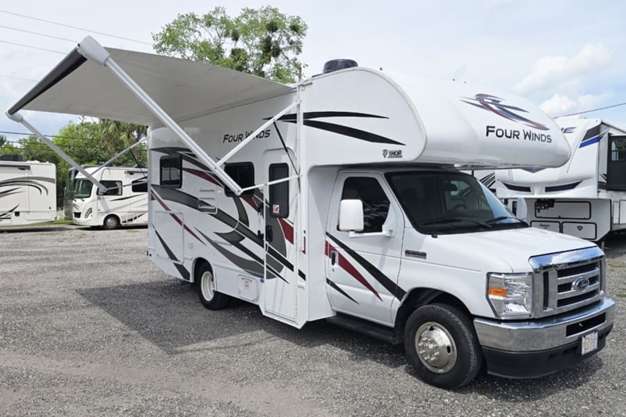 White Thor Four Winds motorhome with extended awning for rv rental, parked on gravel.