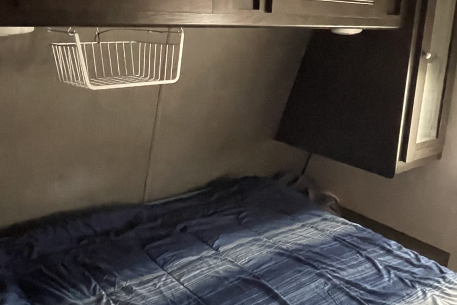 Cozy RV rental bedroom with dark wood cabinets, a blue striped bed, and a wall-mounted TV. Compact and functional.