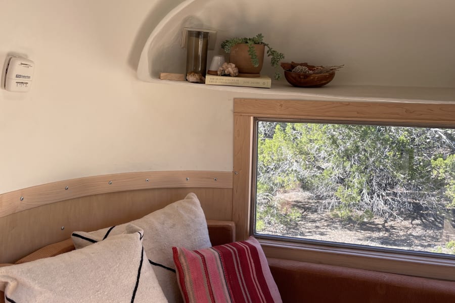 Cozy RV rental interior with plush seating, natural wood accents, and a built-in shelf displaying plants & decor. Enjoy the view!