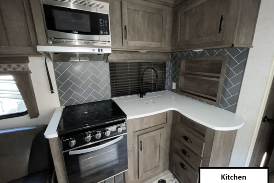 Modern RV rental kitchen with stainless steel microwave, oven, sink, and stylish gray herringbone backsplash.