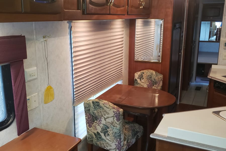 Cozy RV rental interior showing a dining area with floral chairs, a wooden table, and part of the kitchen.