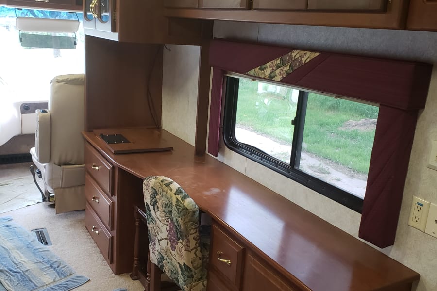 Explore this well-appointed RV rental interior featuring a large desk area, comfy chair, and overhead cabinets for storage.