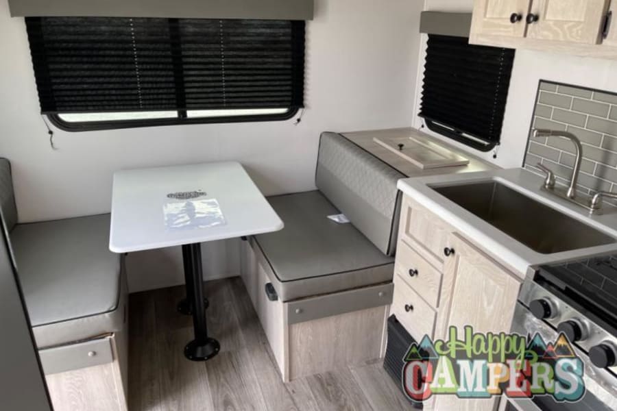 RV rental interior: cozy dinette with table, benches, and a compact kitchen featuring sink & stove. Bright, functional space.