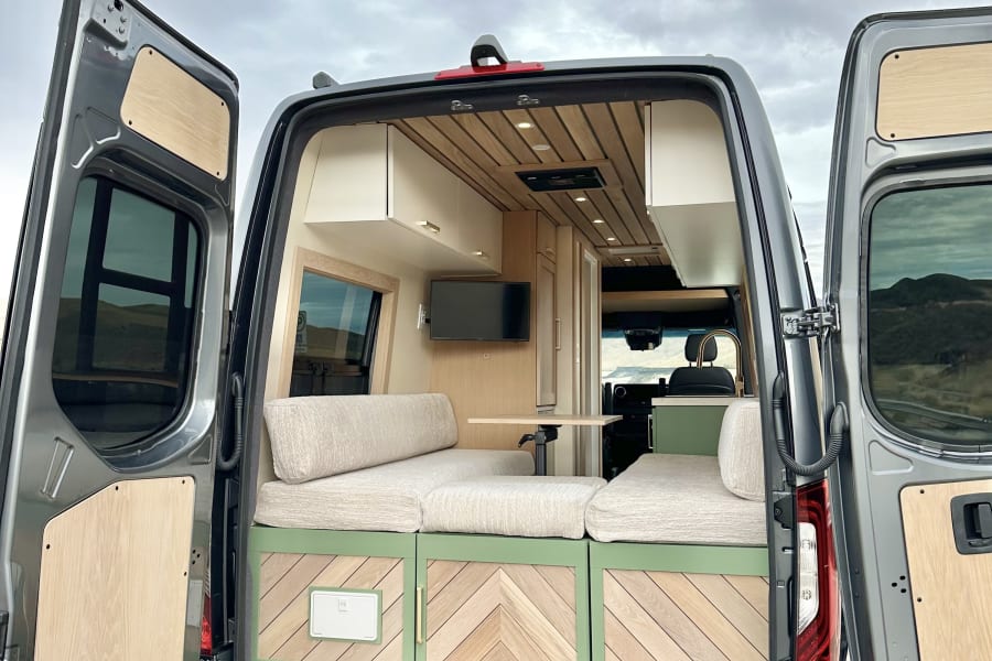 RV rental: Step into this custom grey camper van. Its chic interior features light wood, green storage, and comfortable seating.