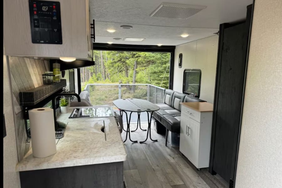 Cozy RV rental interior with kitchen, dining, and a rear patio deck opening to forest views. Perfect for camping adventures.
