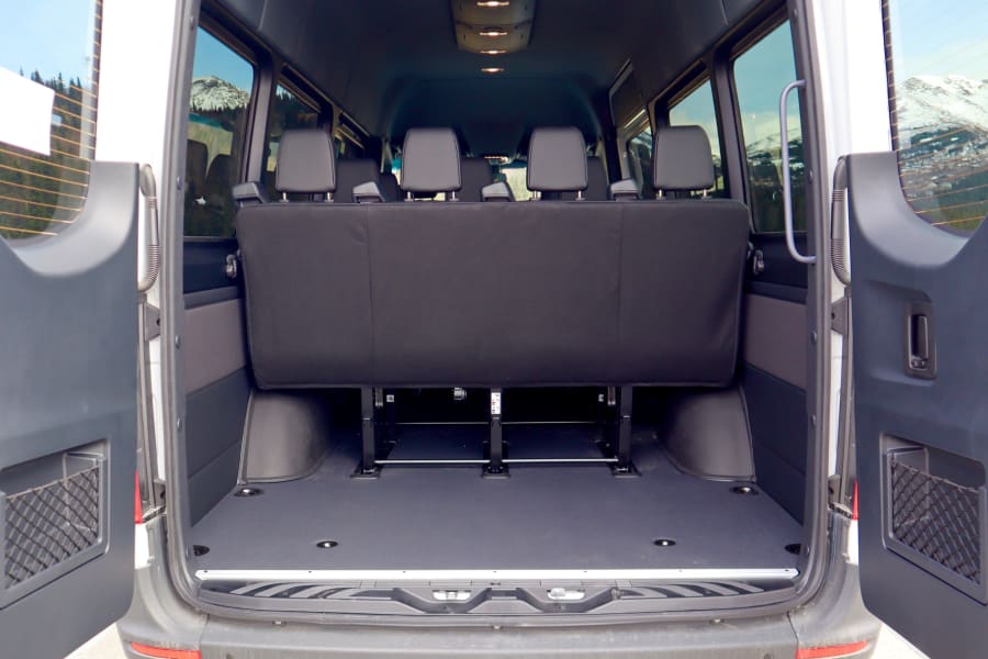 RV rental van interior with open rear doors, showing bench seats and a scenic mountain view.