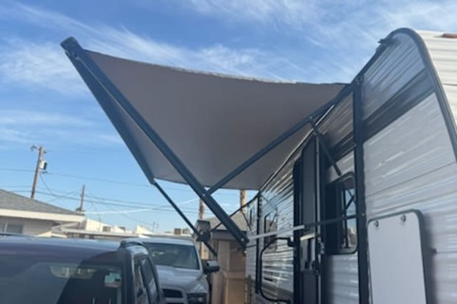 Bright sky over an RV rental, a travel trailer with its awning extended & steps down, parked for adventure.