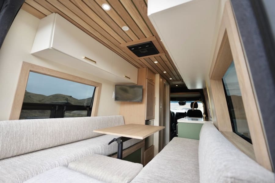 Inside a bright **rv rental**: cozy dinette, wood ceiling, kitchen, and scenic window views perfect for adventure.