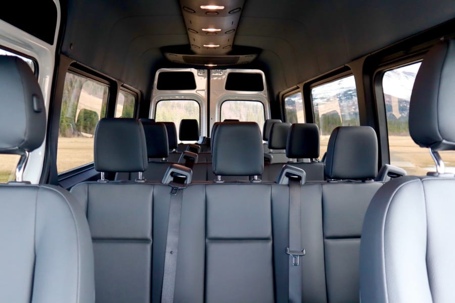 Spacious interior of an RV rental passenger van, featuring multiple rows of black seats and scenic mountain views through windows.
